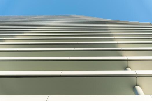 A perspective shot looking up at the facade of a modern building, featuring horizontal lines and a clear blue sky. The image emphasizes symmetry, minimalism, and architectural design. photo
