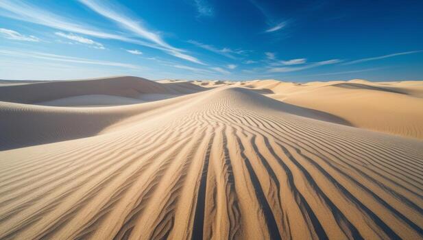 Desert landscape showcasing sand dunes with linear patterns and a bright blue sky photo