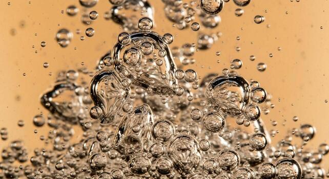 Close up of numerous clear bubbles rising and merging within a viscous golden liquid creating dynamic abstract patterns photo
