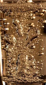 Close up abstract view of shimmering golden bubbles rising and swirling within a clear liquid creating a dynamic visual effect photo