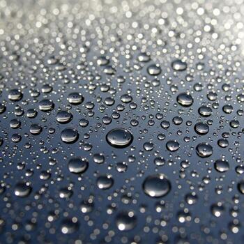 Close up macro photograph of numerous small water droplets scattered across a dark reflective surface creating a textured pattern photo
