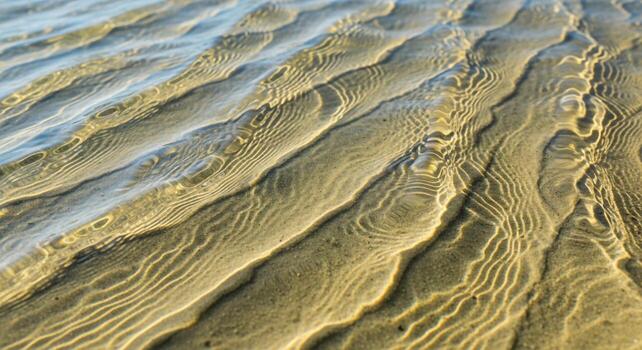 Sunlight dances on rippling sand beneath clear shallow water creating mesmerizing abstract patterns and textures photo