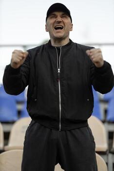Man in black bomber jacket and cap cheers enthusiastically during important game in empty stands photo