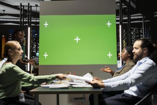Business partners in a briefing session late at night with mockup screen in enterprise office after hours, discussing project agenda and targets. Diagrams to predict development outcomes. photo