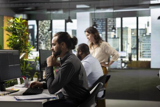 Male professional in a corporate workspace coordinates tasks and objectives. Employee reviews files, projections and business intel to drive progress and resource allocation for company. photo