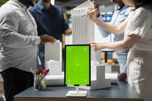 Engineers team share master plan ideas next to chroma key display, using 3D architectural models and blueprints for construction layout details. Modern design city planning in a session. photo