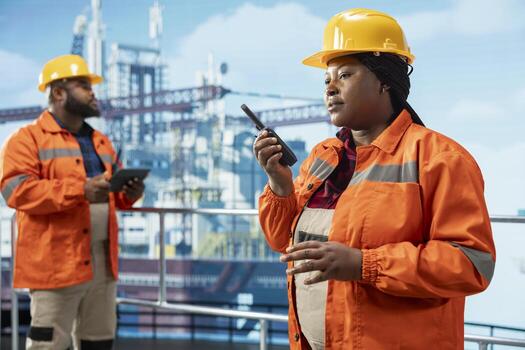 Offshore platform professional using hand portable radio device to coordinate workflow during operations. African american drilling rig worker speaking in walkie talkie, doing emergency procedures photo