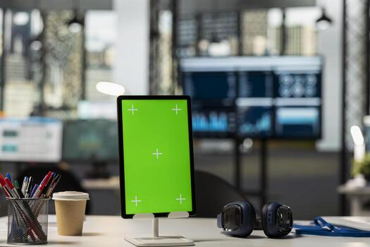 Empty modern office desk with tablet displaying green screen template. Digital device on table in vacant workplace with isolated copy space for financial content or company branding. photo