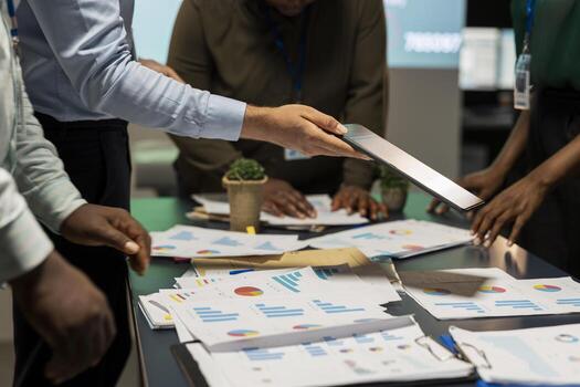 Close up of business people prepare for a pitch by reviewing financial data on documents inside the boardroom after hours. Exchanging reports and delivering forecasting updates for management. photo