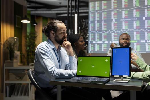 Diverse coworkers collaborates for a meeting at night with a green screen device, analyzing numbers and aligning project goals. Discuss growth strategy in an executive brief after hours. photo