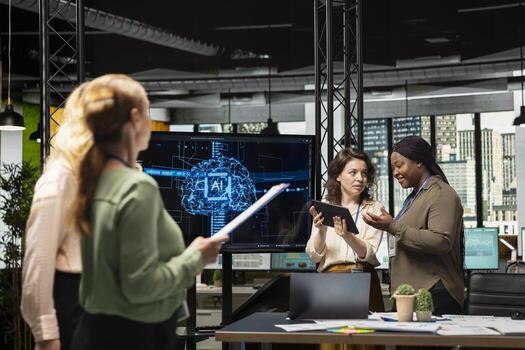 Powerful team of diverse associates review analytics from TV monitor, applying machine learning tools and neural networks to drive development and achieve corporate goals. photo