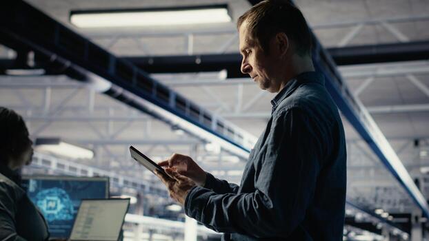 IT expert in server hub uses tablet to optimize deep learning AI systems handling tasks. Data center programmer adjusts artificial intelligence model parameters using device, camera B photo