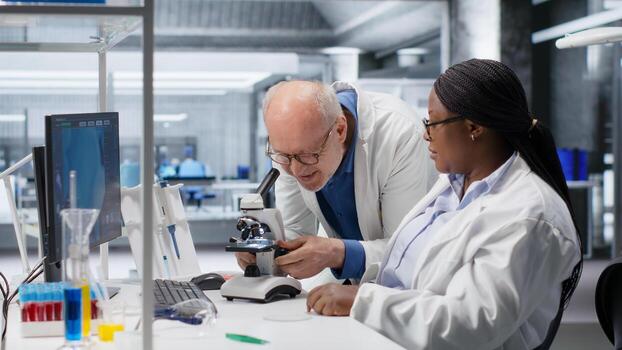 Researcher using microscope and specimen tray in laboratory workspace. Optical instrument, lens system and magnifying glass support clinical testing and biotechnology for healthcare. photo