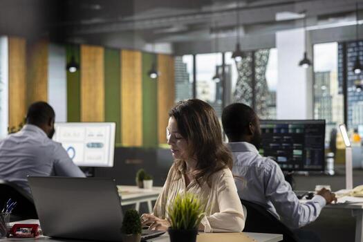 Business people gathered around laptops working on project tasks and targets for development. Office environment promotes synergy, teamwork and insight through analytics and planning. photo
