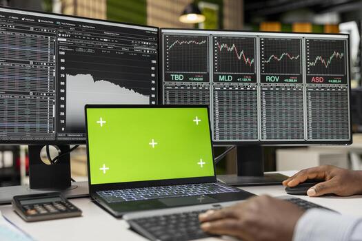 Close up of prop firm trader using green screen laptop on desk and computer displaying stock market candlestick graphs. Financial expert uses chroma key notebook and PC showing stock exchange assets photo