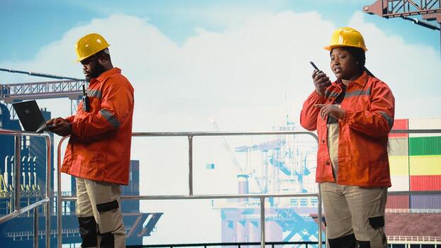 Drilling rig worker using walkie talkie enabling quick response coordination, performing maintenance. Engineer listens to status report through handheld radio, managing logistics, photo