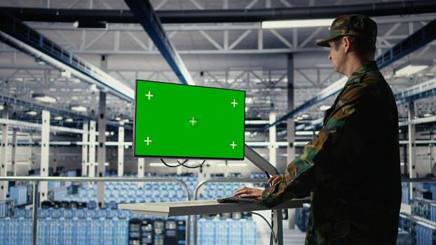 Military data center professional using software on green screen mockup PC to detect enemy threats. Army man in data center uses chroma key computer to detect issues , camera A photo