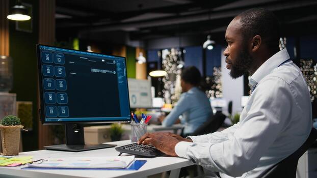 African american male checking web AI chatbot responses for some tasks, working after hours to meet business objectives. Problem solving with futuristic tech and machine learning. photo