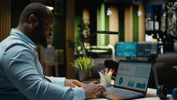 Black business consultant working late at night on proofreading documents, writing reports on laptop. Creating a summary and designing strategy to align with company objectives. photo