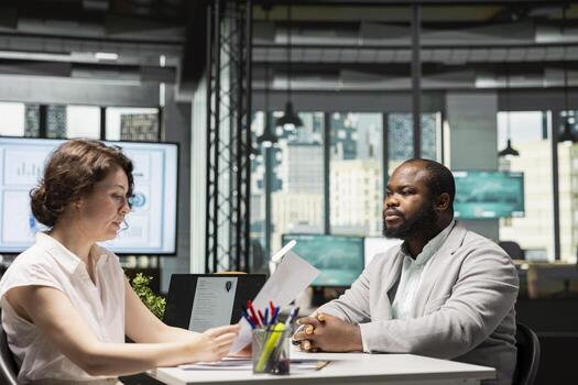 Black confident applicant discusses resume presentation with HR manager during job interview in a corporate workspace, focusing on career development with his qualifications. Potential employment. photo
