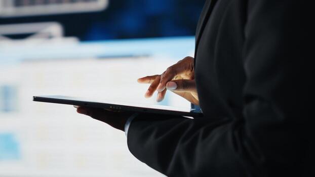 Close up of businesswoman using tablet to compare company KPIs data on digital videowall before making decisions. Entrepreneur analyzing key performance indicators using device app photo