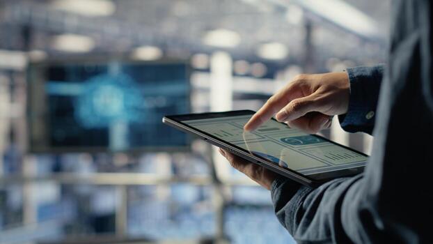 Server room employee checks data charts on tablet to monitor system health. System administrator reviews graphs to make sure data center meets business goals and client needs, camera B photo