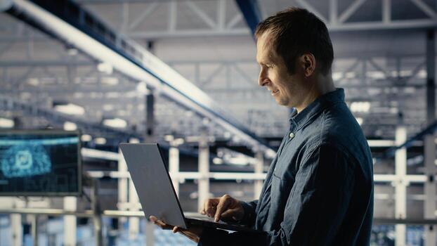 Data center IT professional deploys deep learning software on infrastructure racks. Server farm engineer trains AI systems with datasets using laptop to support applications, camera B photo