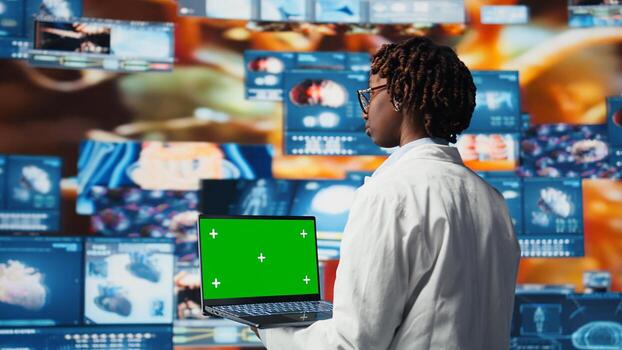 Green screen laptop used by healthcare expert looking at CT scans, MRI data, and lab analytics on videowall. Scientist in medical research lab reading health data with mockup notebook, camera A photo