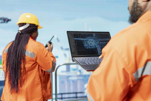 Close up of engineering team on offshore platform using artificial intelligence software on laptop to optimize drilling operations. Teamworking colleagues monitoring barge activity using AI photo