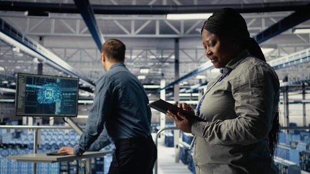 Data center employee monitoring infrastructure processes, reviewing operational metrics. Server room IT worker reviews high tech infrastructure equipment rigs reports during inspection, camera A photo