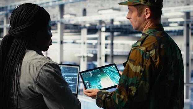 Army commander and software developer in data center integrating AI into radar systems for missile tracking. Soldier and female programmer in server hub analyzing aerial movement on laptop, camera B photo