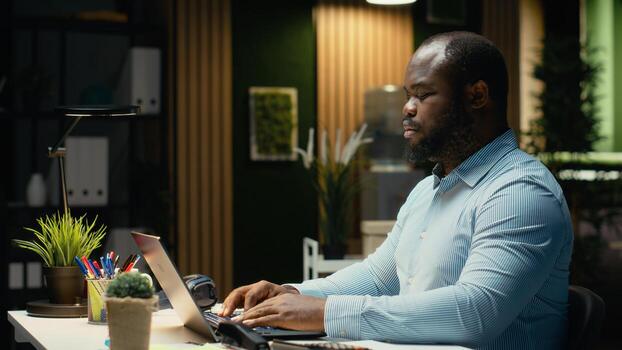 Portrait of black male analyst smiling and working late after hours, reviewing data insights to meet business goals, solving budgeting tasks at night and fact checking documents. photo