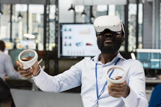 Male corporate employee using VR headset and wireless controllers, interacting with 3D virtual data and numbers. Black man working in modern high tech IT company with futuristic digital technologies. photo