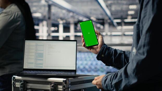 Server room software developer using mockup phone while waiting for updates to finish installing. Data center engineer uses green screen smartphone, waiting for code to finish compiling, camera B photo