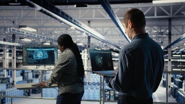 Data center software developer using AI LLM chatbot suggestions to adjust rigs system settings. Server hub IT professional using large language model on laptop to manage infrastructure, camera A photo