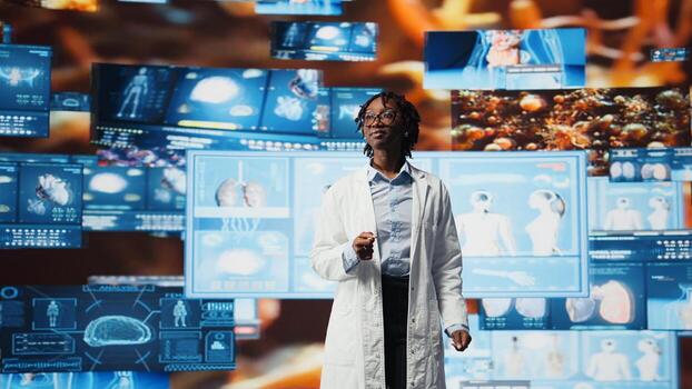 Smiling doctor in lab coat pleased by medical research data while monitoring interactive dashboards. Happy clinician satisfied with medical reports on multimedia wall, camera A photo