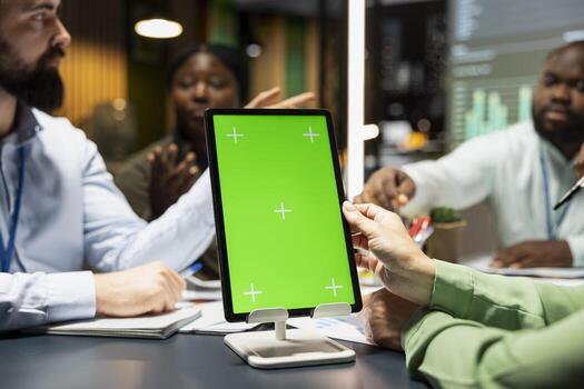 Multiethnic team of experts in a meeting with a chroma key tablet, analyzing analysis numbers and establishing project objectives. Meeting growth goals in a brief late after hours. photo