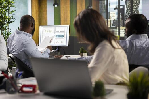 Coworkers in a multinational company greeting each other in office, engaged in solving daily tasks with documents and diagrams. Professional diverse work team discusses corporate goals. photo