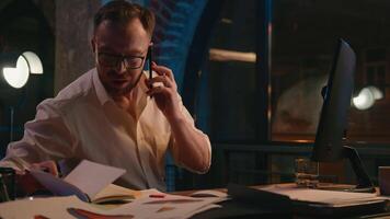 caucasico uomo attività commerciale tipo uomo d'affari maschio nel buio notte sera ufficio opera multitasking parlando mobile Telefono discutere dai un'occhiata ricerca dati nel taccuino lavoro d'ufficio pc computer navigazione occupato multitask video