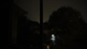 se av fönster med stolpar och glas med regndroppe. blinkande lighte av åskväder ljus upp de himmel . stänga upp skott från inuti de byggnad video