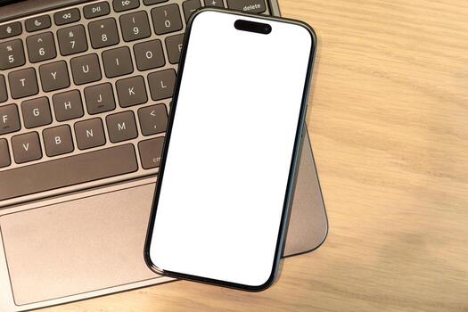 Smartphone with Blank Screen Resting on Laptop Keyboard, Digital Workspace and Connectivity. mobile apps, website designs, mockups, digital content. remote work, technology and design. photo