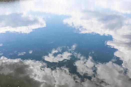 Calm water surface. Summer evening near a forest lake, the surface of the water is smooth, with small waves. The sky with clouds is reflected from the surface, coloring the water in different colors. photo