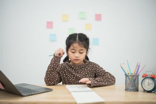 Young girl engaged in creative learning with notebook and colored pencils at a study table surrounded by sticky notes and a laptop, focused on her tasks photo