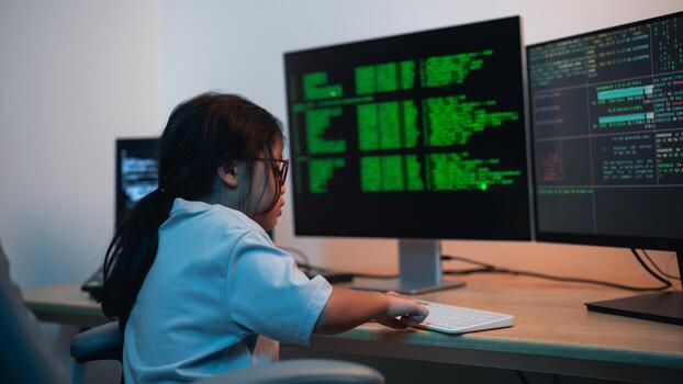 Young girl focused on coding and programming at computer desk with dual monitors displaying green text on black screens in modern tech environment photo