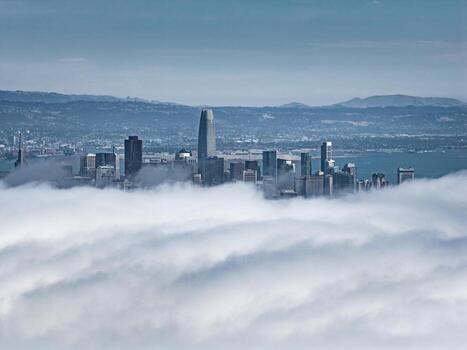 Aerial view of San Francisco's skyline partially covered by fog, featuring the Salesforce Tower, skyscrapers, and distant hills in the background. photo