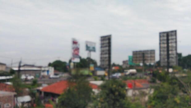 This softly blurred photo captures an urban scene with tall buildings, billboards, and red-roofed houses in the foreground.