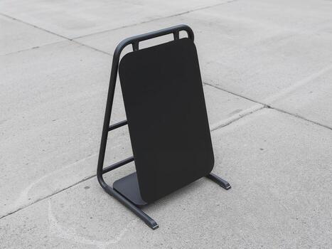 Blank black A-frame sign mockup standing on a concrete floor. Empty vertical sandwich board for menu or message display. photo