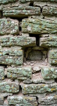 Close up view of an ancient weathered stone wall with green moss and lichen growth showing its age and texture photo