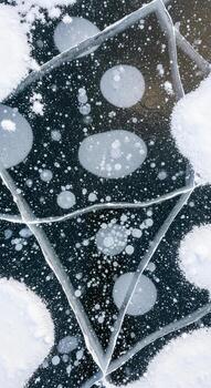 Intricate patterns of frozen bubbles trapped within cracked ice formations on a dark surface photo