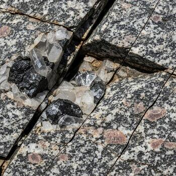 Close up view of a speckled granite surface with dark mineral veins and subtle pinkish inclusions creating a natural abstract pattern photo